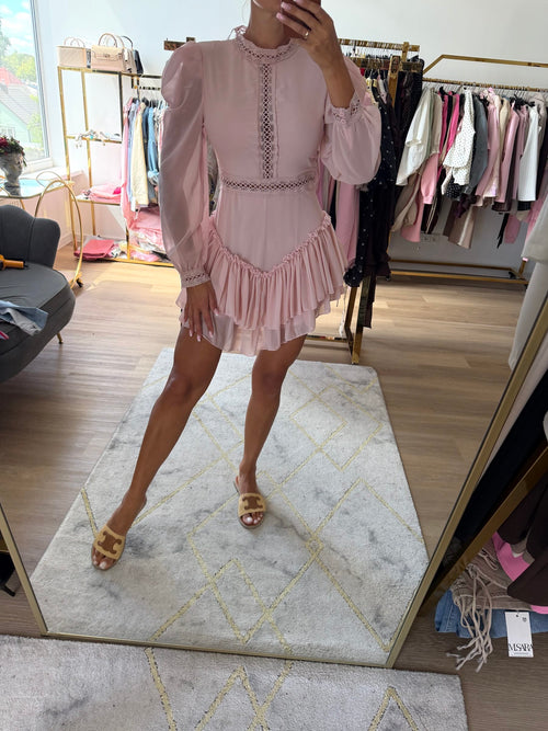 Švelniai rožinė elegantiška mini suknelė su ilgomis permatomomis rankovėmis, nėrinių detalėmis ir raukinių sijonu.